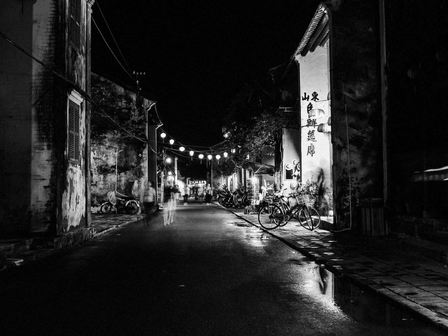 A narrow street at night lit by a string of bulbs
