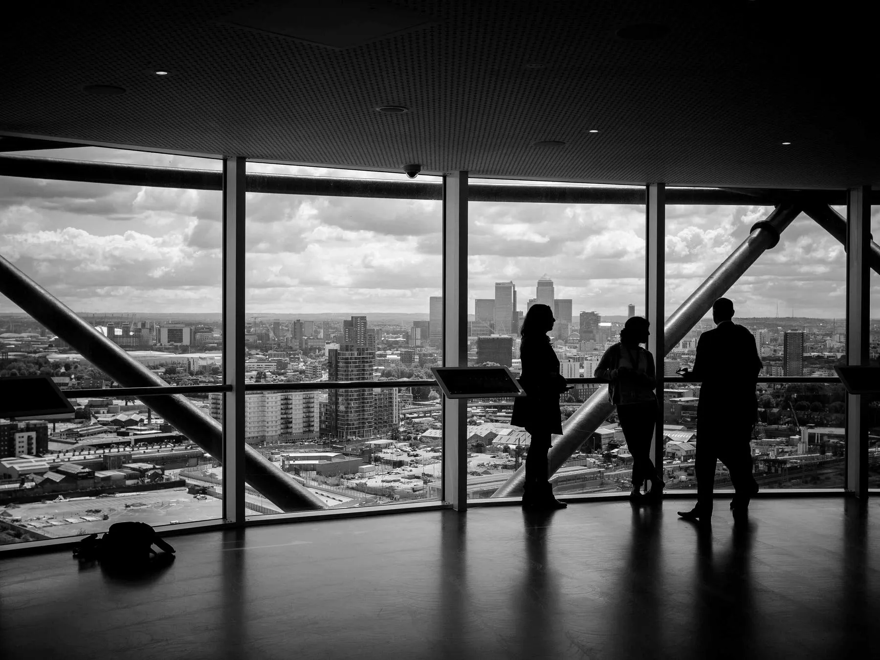 Silhouettes of three people at a tall window overlooking a city
