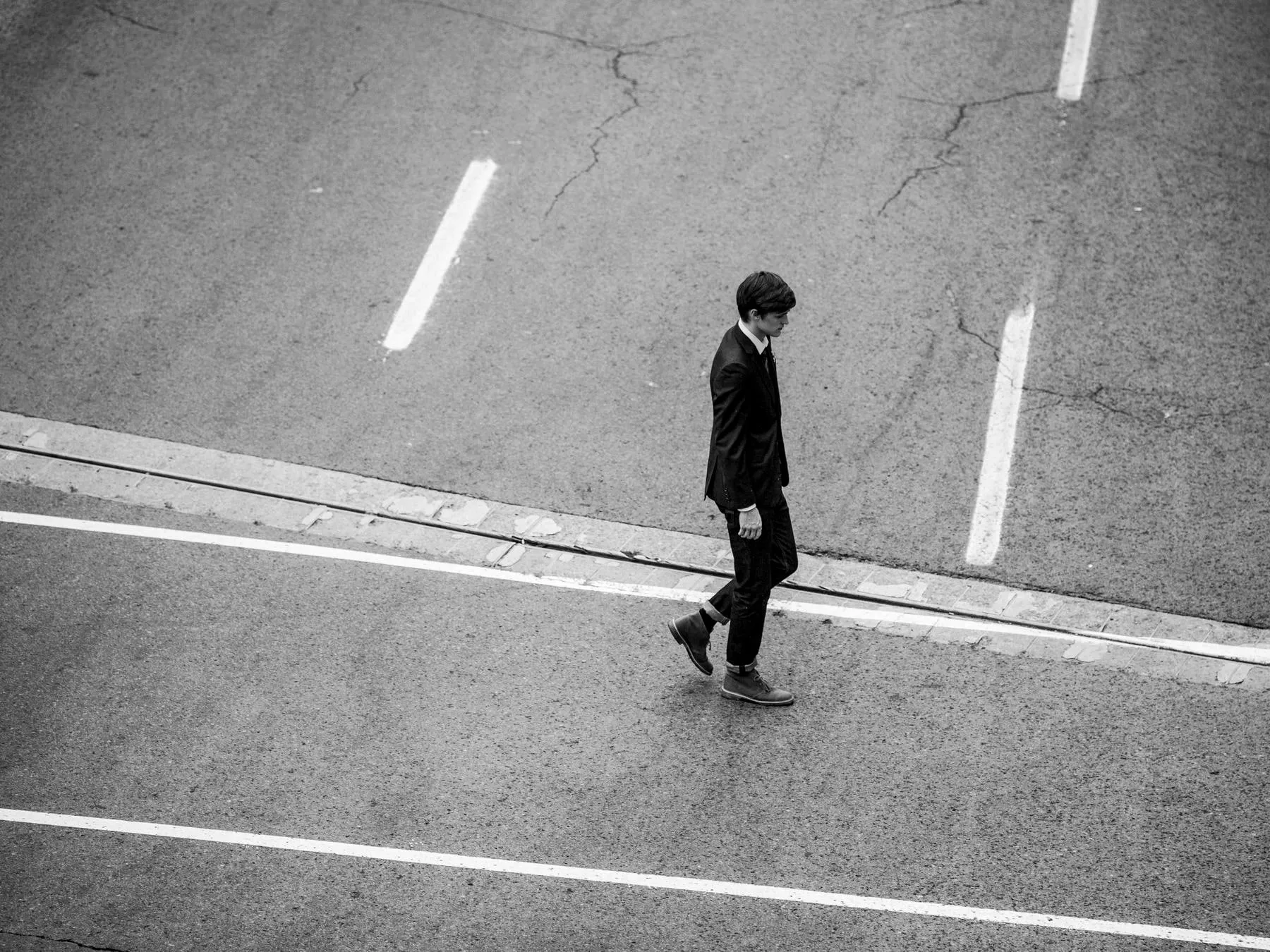A man in a dark suit crossing an empty road