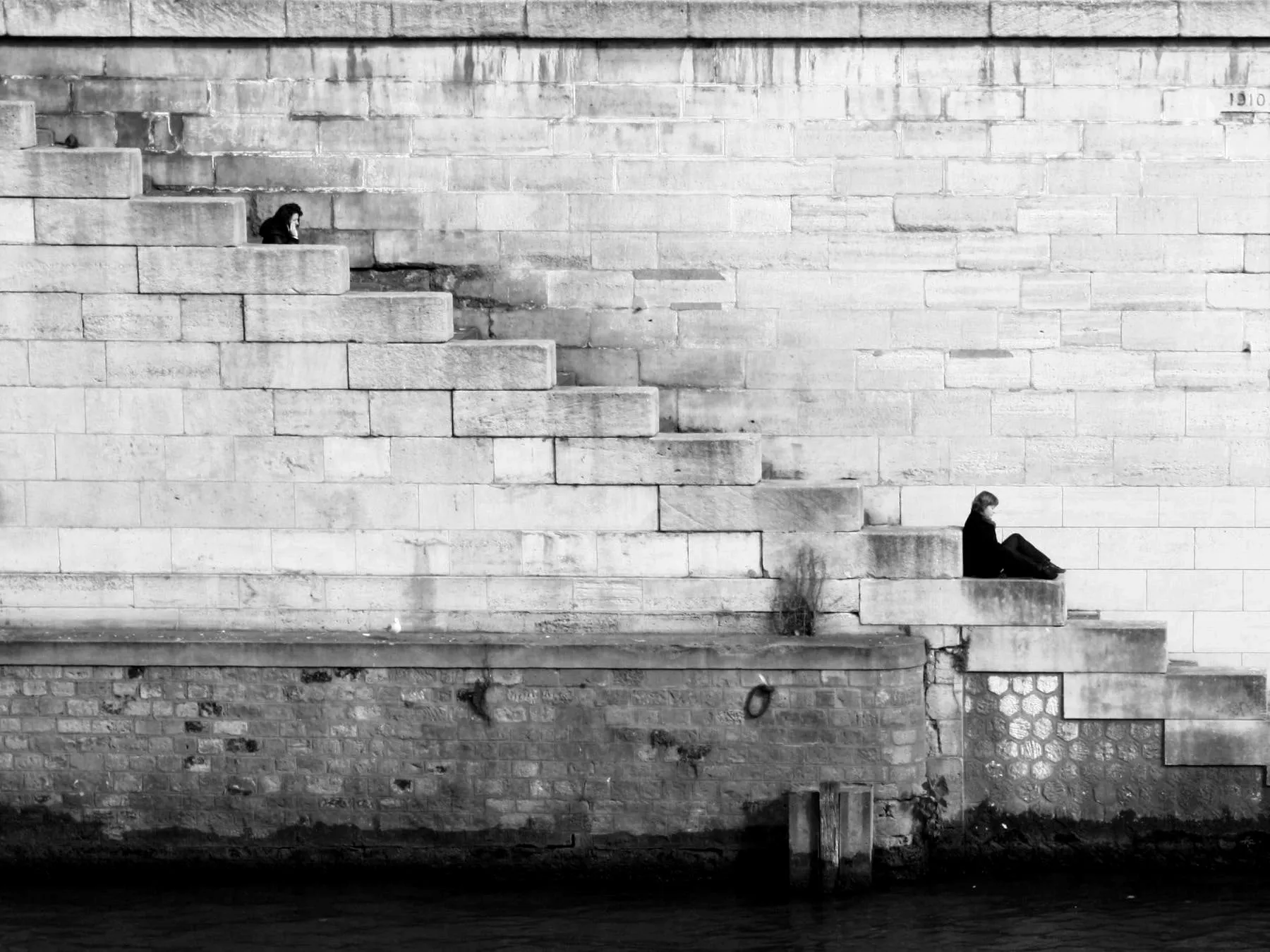 A lone figure seated at the foot of pale stone steps