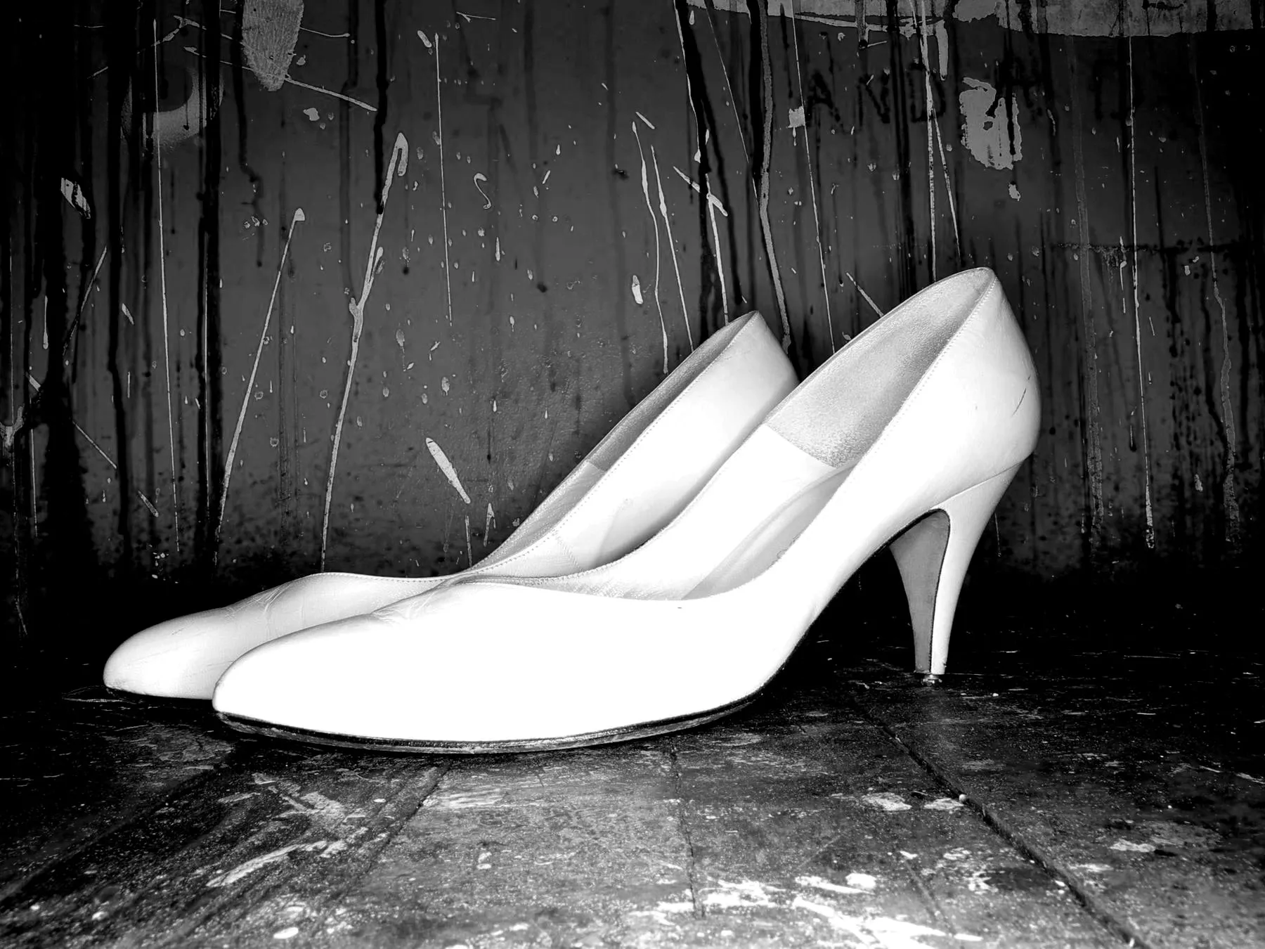 A pair of white heels against a dark timber wall
